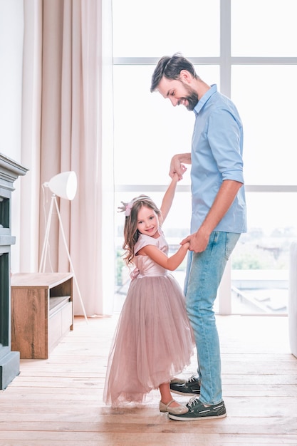 Daughter standing on fathers shoes while dancing in living room