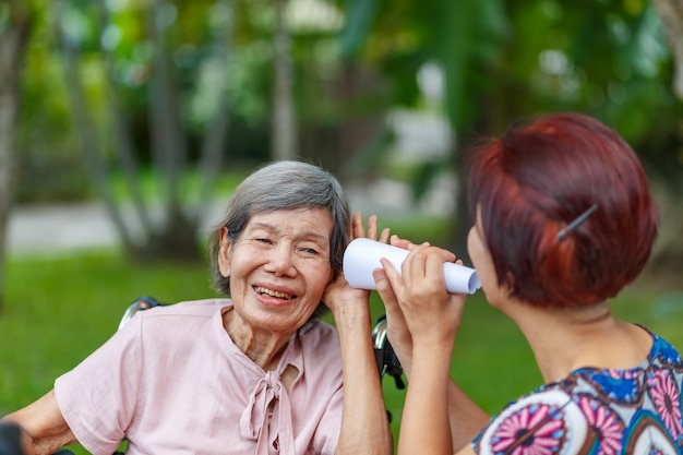 Daughter talking to hearing impaired elderly woman , using
paper tube