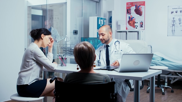 Daughter talking with doctor about recovery for elderly mother in wheelchair. Dsabled disability handicapped old person treatment in modern private hospital or clinic. Medicine and health care system