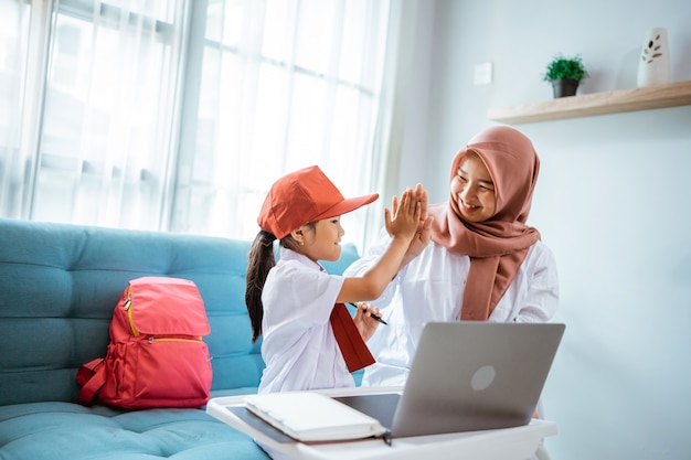 Daughter with school uniform highfive with mother during online class at home