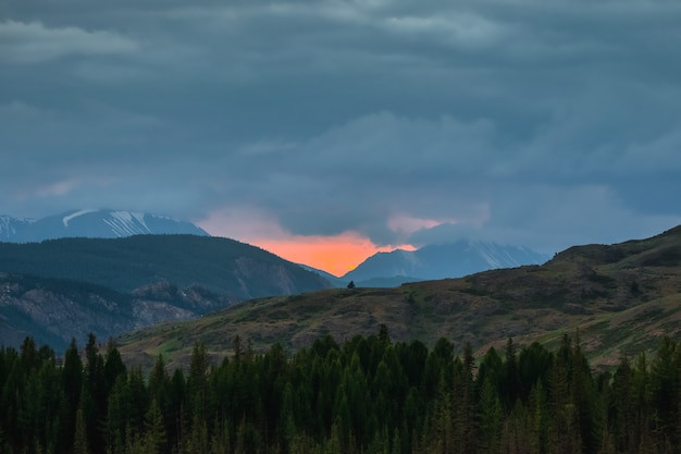 Alba in montagna. paesaggi naturali colorati con tramonto o alba. paesaggio atmosferico con sagome di montagne con alberi sullo sfondo del cielo arancione dell'alba.