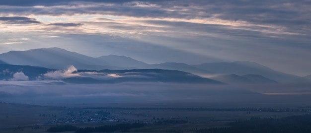 Dawn in the mountains, peaks above the clouds, foggy