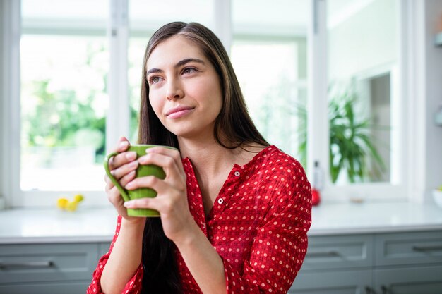 Day dreaming brunette holding cup in kitchen