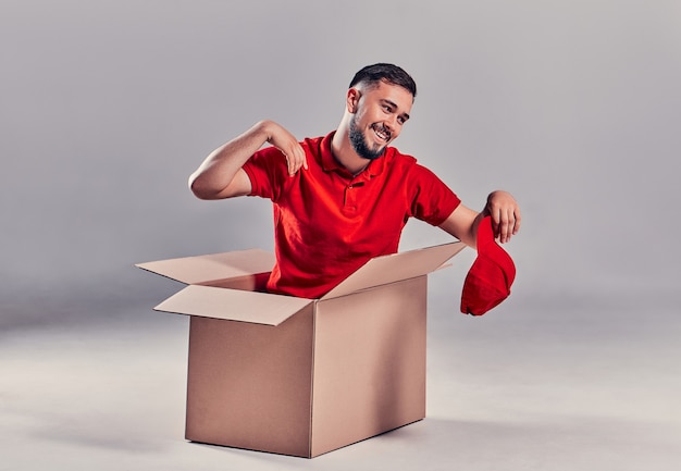 Day moving. Delivery of goods from shopping in the online store. Loader or courier sitting in box and  tired against gray background.