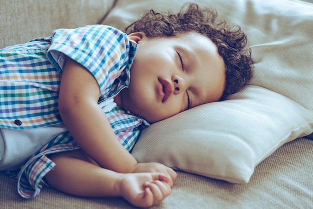Giorno di sonno. piccolo bambino africano che dorme sdraiato sul divano di casa