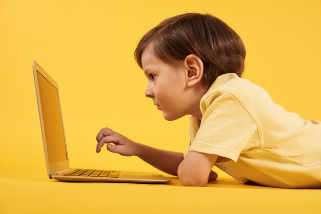 Daydreaming boy with laptop lies on floor on yellow flour.