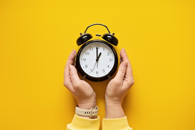 Daylight saving day fall back black alarm clock and female hands on yellow background daylight