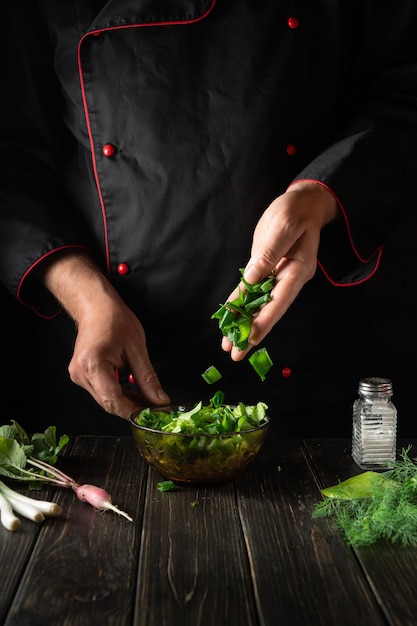 добавление нарезанного зеленого лука в салат из свежих овощей руками шеф-повара на кухне
