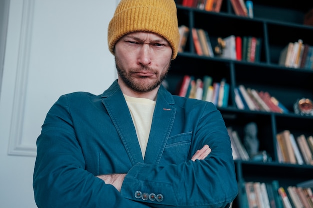 De aantrekkelijke volwassen gebaarde boze mens hipster in gele hoed bekijkt camera