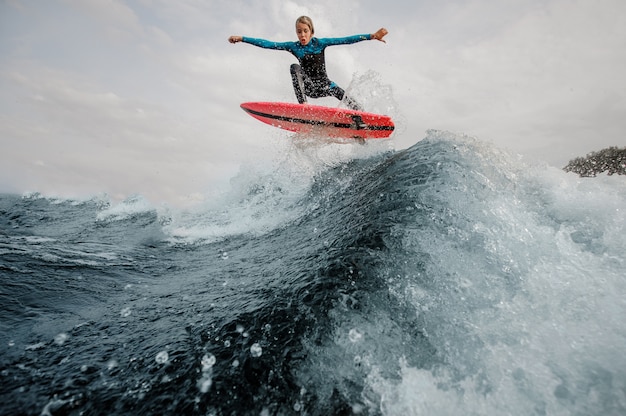 De actieve kindjongen kleedde zich in zwempak surfen die omhoog op oranje raad springen