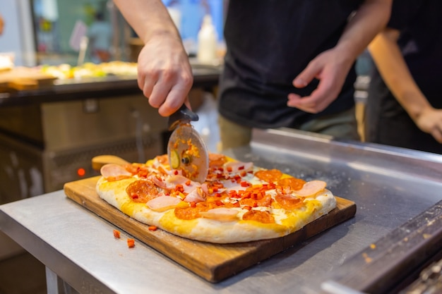 De afgewerkte pizza snijden met mannelijke handen met een mes