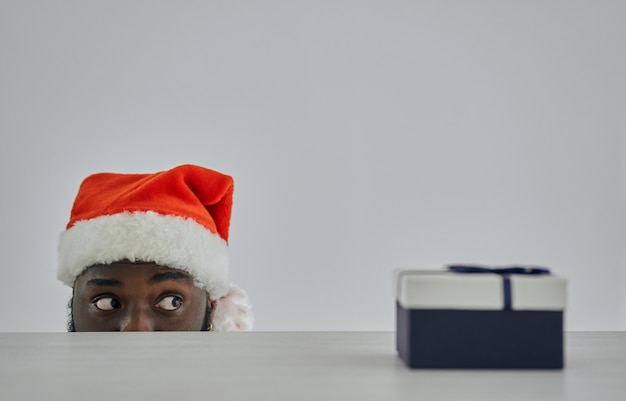De Afrikaanse man met de kerstmuts kijkt toe vanaf de tafel met een cadeau