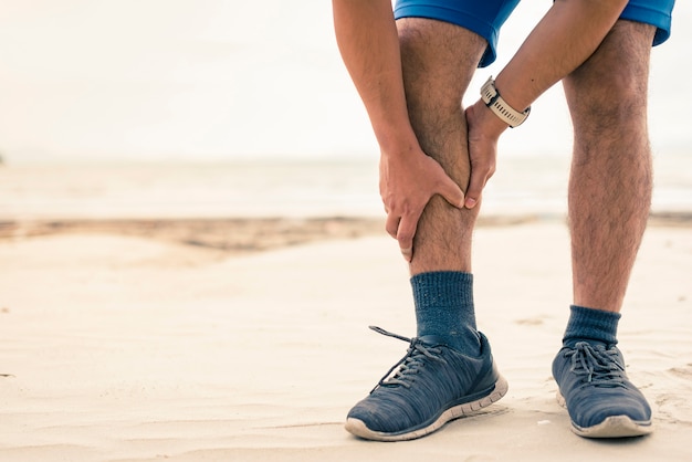 De agent van de mens houdt zijn sporten gewonde been op de strandachtergrond