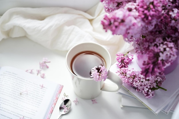 Foto de ansichtkaart is prachtig een mok thee, een oud boek en een boeket paarse lila een prachtig stilleven lentetijd het concept van goedemorgen