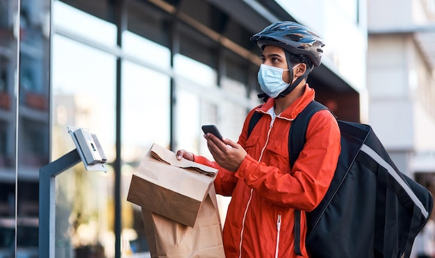 De app bracht me naar dit adres. Shot van een gemaskerde man die zijn mobiel gebruikt terwijl hij eten bezorgt