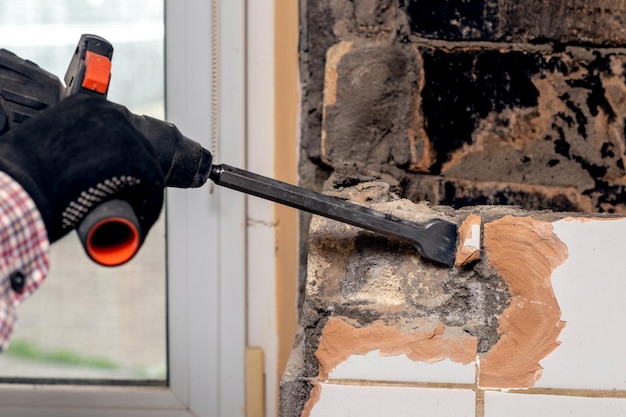 De arbeider ontmantelt met behulp van een perforator de schoorsteen de muren in de kamer