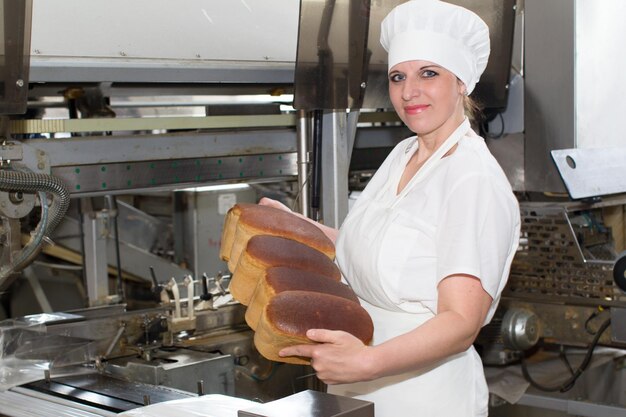 De arbeider van de fabriek voor de productie van brood met brood in haar handen
