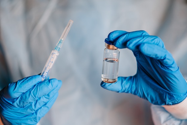 De arts, de verpleegster, de wetenschapper dienen blauwe nitrilhandschoenen in die vaccin en spuitinjectie houden. Gebruik voor preventie, immunisatie en behandeling van coronvirusinfectie.