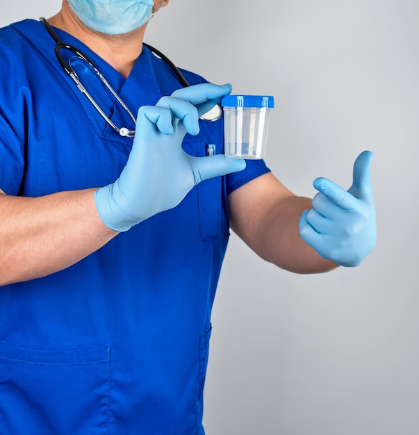 De arts in blauwe eenvormig en latexhandschoenen houdt een lege plastic container voor het nemen van urinesteekproeven