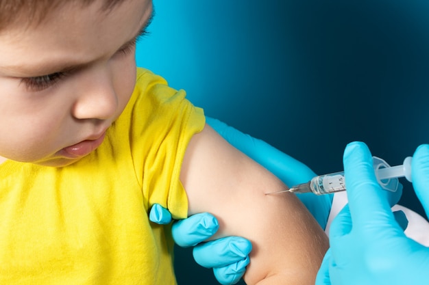 Foto de arts of verpleegkundige injecteert het kind in de arm in de schouder.