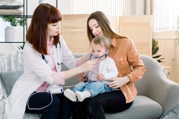 De arts van de vrouw houdt een inhalator van de maskerdamp voor weinig babymeisje. behandeling van astma. ademen door een stoomvernevelaar. concept inhalatietherapieapparaat.