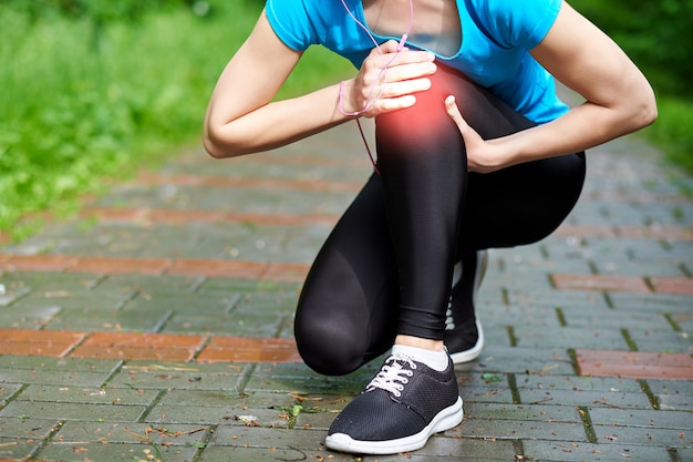 De atleetagent van de vrouw wat betreft knie van pijn, geschiktheidsvrouw die in de zomerpark lopen. gezonde levensstijl en sport concept