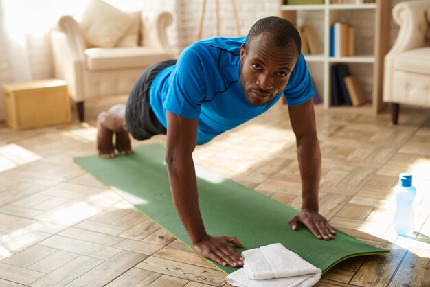 De atletische zwarte mens voert thuis plank op mat uit.