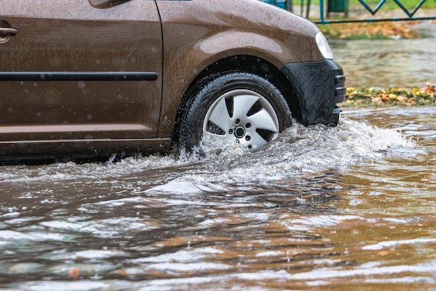 De auto rijdt door een plas in zware regen Spatten van water onder de wielen van een auto Overstromingen en hoog water in de stad