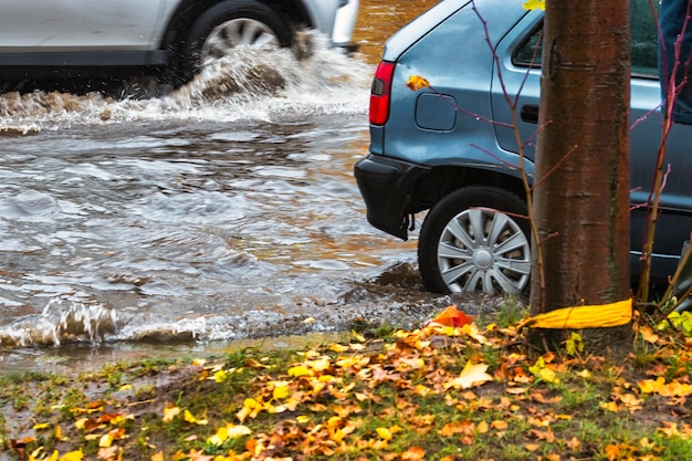 De auto rijdt door een plas in zware regen Spatten van water onder de wielen van een auto Overstromingen en hoog water in de stad
