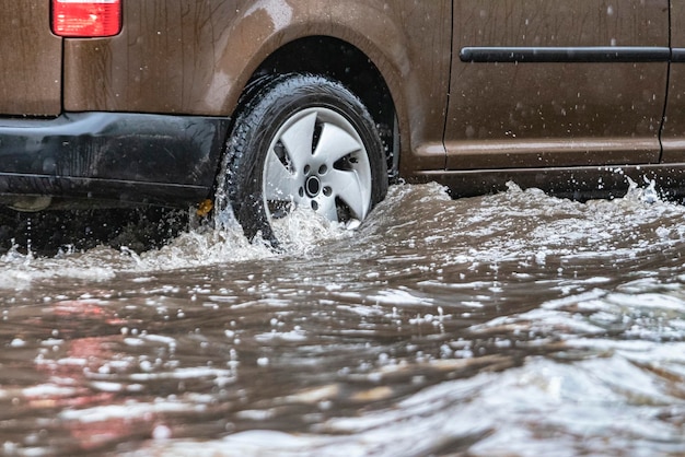 De auto rijdt door een plas in zware regen Spatten van water onder de wielen van een auto Overstromingen en hoog water in de stad