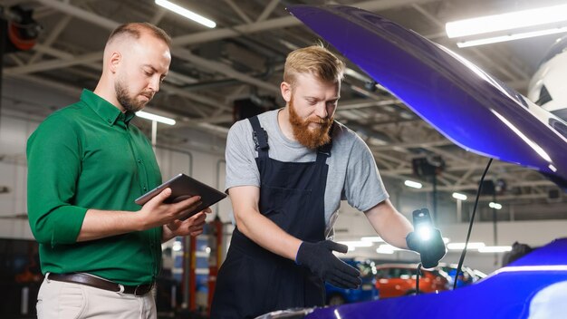 De autoservicemanager schrijft de reserveonderdelen die in de auto vervangen moeten worden op de tablet Een automonteur wijst zijn collega op problemen