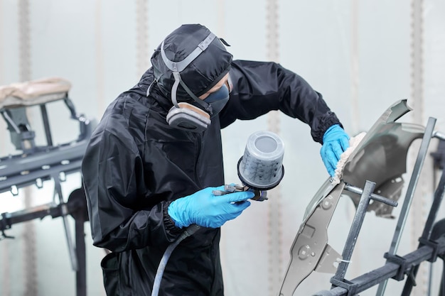 De autovakman is trots op zijn werk terwijl hij een gasmasker opzet en verf aanbrengt in een hightech stand