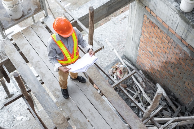 Foto de aziatische documenten van de het projectblauwdruk van de architectenholding en het dragen van helm bij bouwwerf