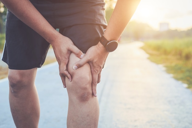 De Aziatische handen van het mensengebruik houden op zijn knie terwijl het lopen op weg in het park