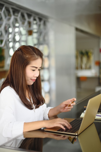 De Aziatische het glimlachen telefoon van de vrouwenholding en het gebruiken van laptop computer om online te winkelen.