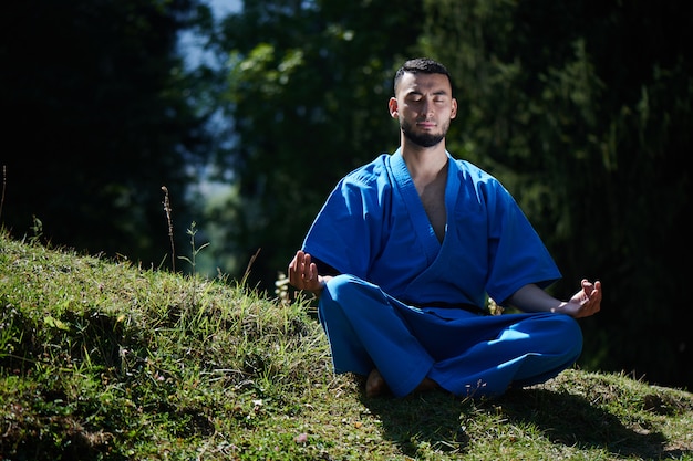 De Aziatische Kazachse karatevechter is mediteert in blauwe eenvormige kimono op een landschap van de de zomer mooi aard
