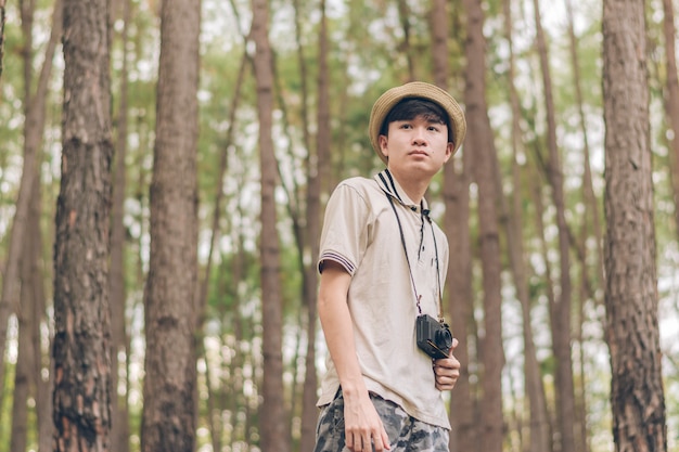 De Aziatische man draagt een shirt, een hoed en een camouflagebroek lopen en nemen foto's in het bos