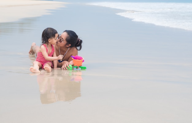 De Aziatische moeder en de dochter spelen samen en kussen op het strand.