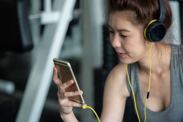 De Aziatische sportvrouw die met oortelefoons aan muziek luisteren voor ontspant na harde trainingoefening in sportgymnastiek.