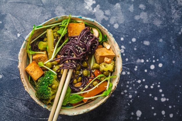 De Aziatische veganist beweegt gebraden gerecht met tofu, rijstnoedels en groenten, donkere achtergrond.