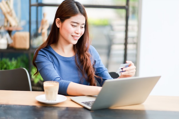 De Aziatische vrouw gebruikend computerlaptop en drinkt het koffiewerk van huisconcept