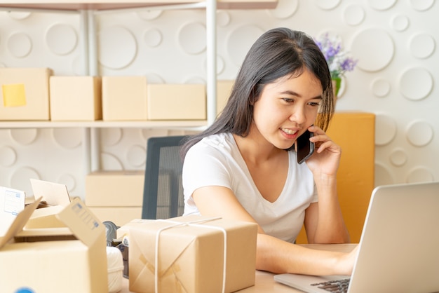 De Aziatische vrouw geniet van terwijl het gebruiken van Internet op laptop en telefoon in bureau