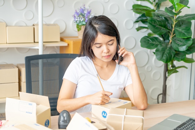 De Aziatische vrouw geniet van terwijl het gebruiken van Internet op laptop en telefoon in bureau