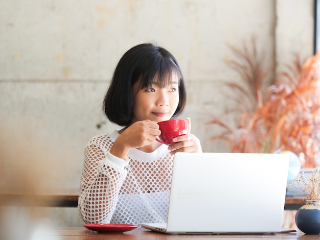 De aziatische vrouw het drinken koffie en ontspant in de koffie van de koffiewinkel