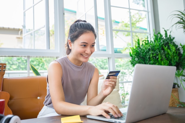 De Aziatische vrouw houdt creditcard en gebruikt smartphone thuis winkelend online.