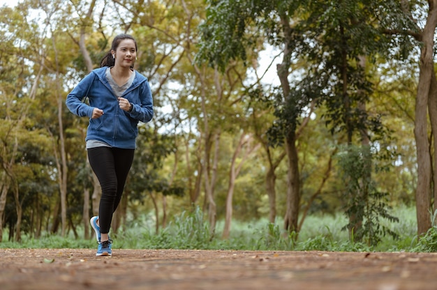 De aziatische vrouw jogt op de weg buiten. Natuurpark. Gezond en levensstijlconcept.