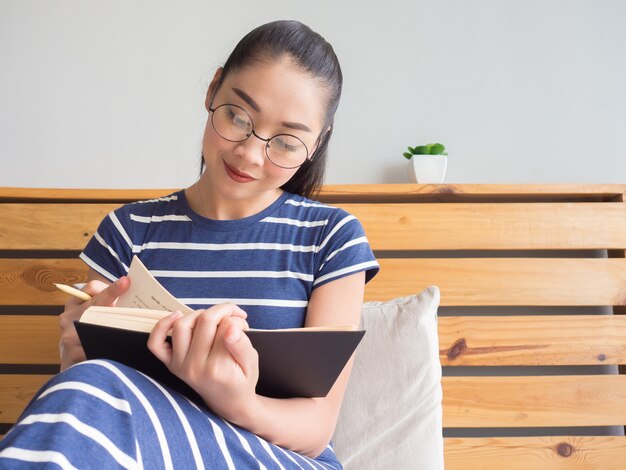 De Aziatische vrouw leest boek op het bed in comfortochtend.