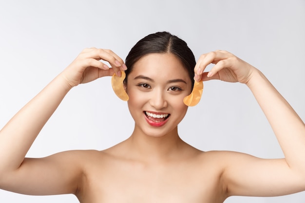 De Aziatische vrouw van de schoonheidstiener geeft haar huid met de gouden vlekken van oogmaskers onder ogen