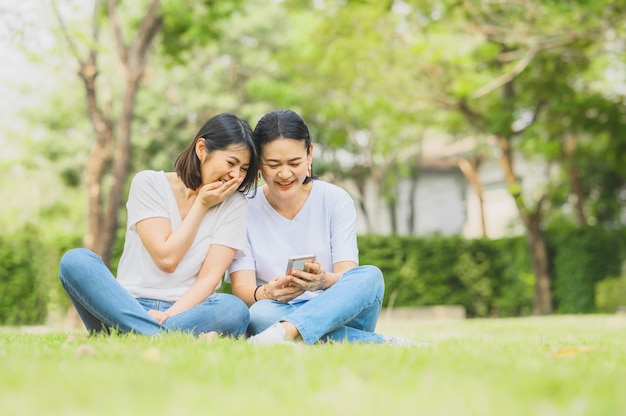 De Aziatische vrouwen lachen terwijl openlucht het gebruiken van smartphone