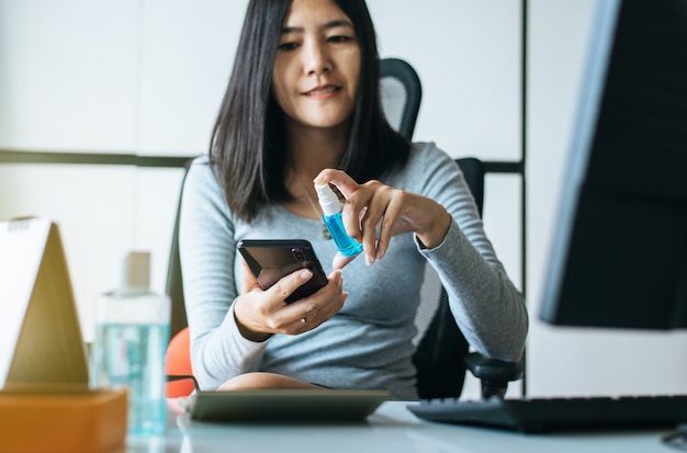 De aziatische vrouwen overhandigen het gebruiken van bespuitende alcohol aan smartphone